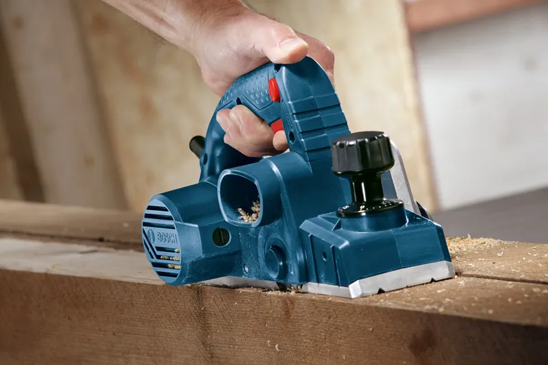 A person uses a blue planer to smooth a wooden board.