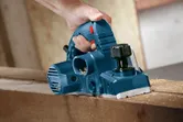A person uses a blue planer to smooth a wooden board.