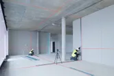 Two workers wearing safety equipment align drywall using a laser leveling tool.