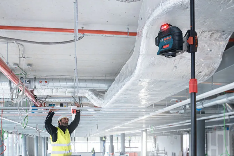A person wearing safety equipment aligns ceiling structures using a laser leveling tool.