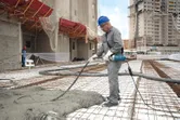 A person wearing safety equipment uses a concrete vibrator on a construction site.