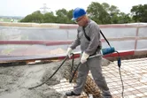 A person wearing safety equipment operates a concrete vibrator on a construction site.