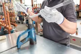 A person wearing safety equipment uses a heat gun to bend a plastic pipe.