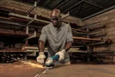 A person wearing safety equipment grinds metal, creating sparks in a workshop.