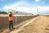 A person wearing safety equipment uses a laser leveling tool with a laser receiver on a construction site.