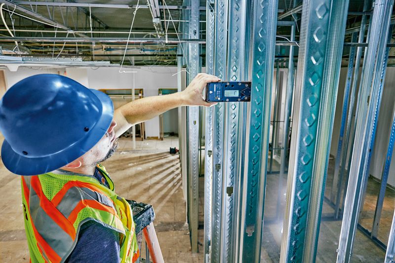 Person wearing safety equipment uses a laser receiver to align metal studs.
