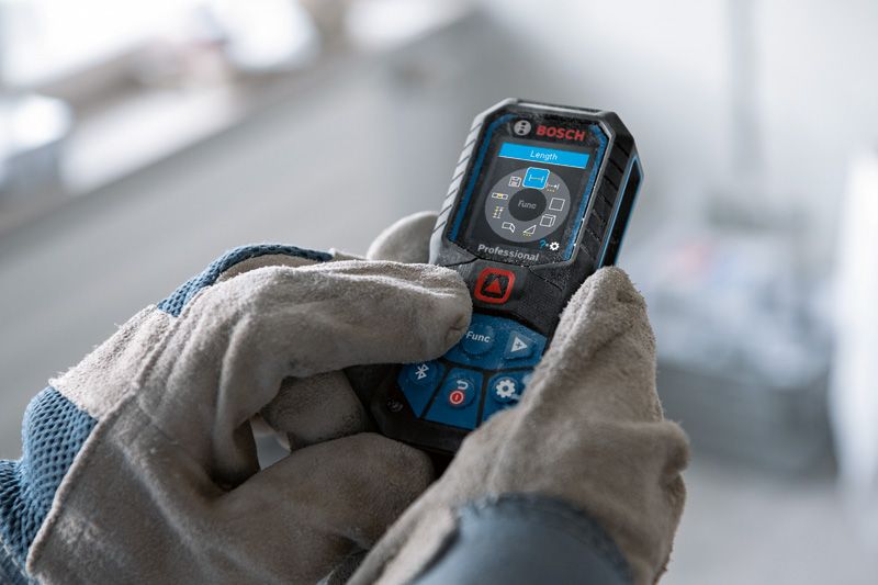 A person wearing safety equipment operates a digital laser measure.