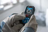 A person wearing safety equipment operates a digital laser measure.
