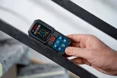 A person holds a laser measure against a metal railing.
