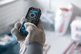 A person wearing safety equipment operates a laser measure in a construction setting.