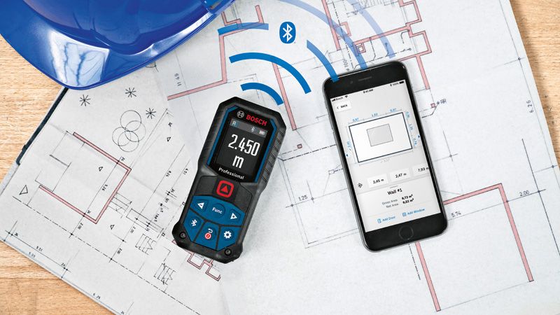 Laser measure syncing data to a smartphone, both placed on architectural blueprints.
