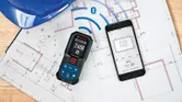 Laser measure syncing data to a smartphone, both placed on architectural blueprints.