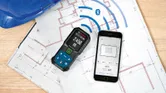 Laser measure and smartphone displaying measurements on architectural plans.