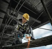 A person wearing safety equipment uses an angle grinder to cut metal scaffolding.
