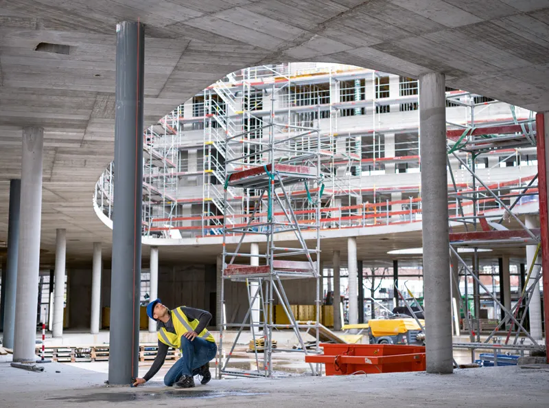 A person wearing safety equipment uses a laser measure to check a column alignment on site.
