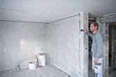 A person measures a wall in a construction site using a laser measure.