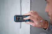 A person uses a laser measure on a concrete wall.