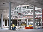 A person wearing safety equipment uses a laser measure to check alignment at a construction site.