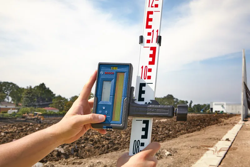 Person adjusts a laser receiver on a leveling rod at a construction site.