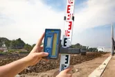 Person adjusts a laser receiver on a leveling rod at a construction site.