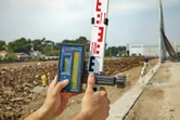 A person adjusts a laser receiver on a grade rod at a construction site.
