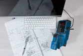 Digital detector connected to a computer beside construction blueprints and a keyboard.