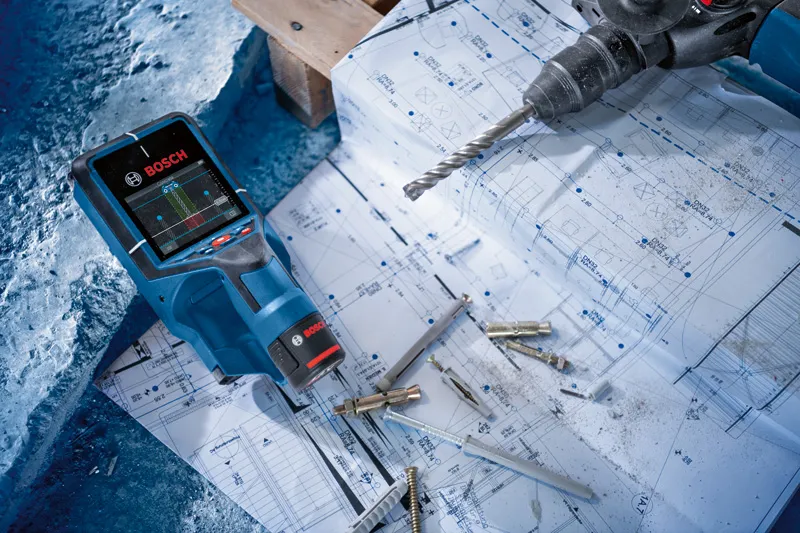 Electronic detector, drill, and fasteners placed on architectural blueprints.