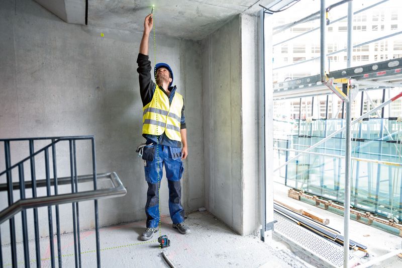 A person wearing safety equipment aligns a laser leveling tool to the ceiling point.