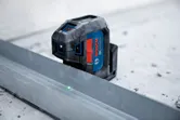 Laser leveling tool projecting green beams onto a metal guide for alignment.