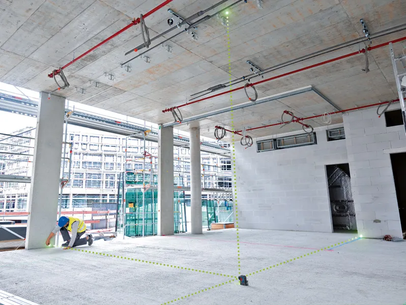 A person wearing safety equipment marks the floor using a laser leveling tool projecting green lines.
