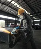 A person wearing safety equipment grinds metal with a power tool in a factory.