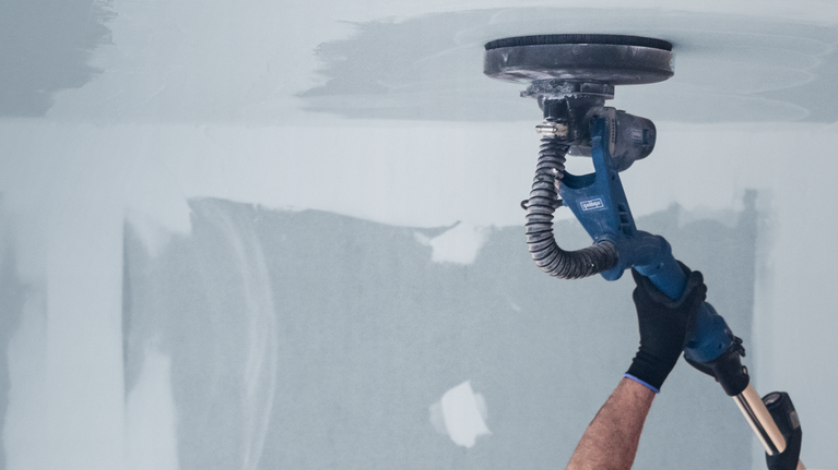 Person using a power drywall sander to smooth a ceiling surface.