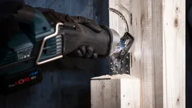 A person wearing safety equipment uses a reciprocating saw blade to cut a wooden beam.