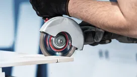 A person wearing safety equipment uses a circular saw to cut a ceramic tile.