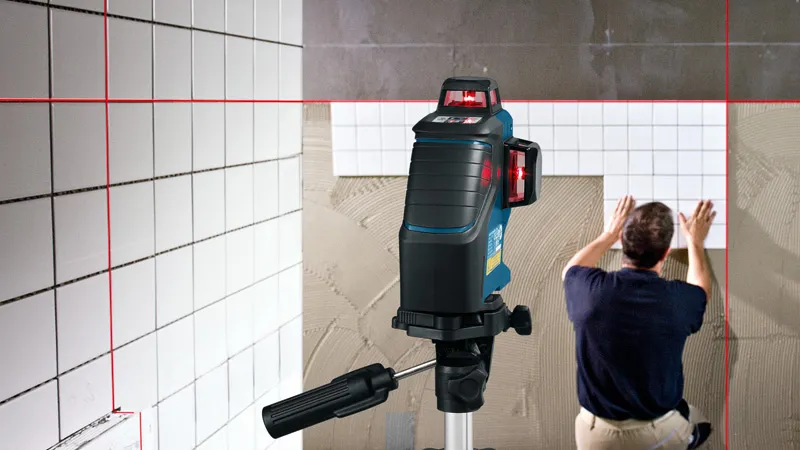 Laser leveling tool projects red lines as a person installs tiles on a wall.