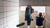Laser leveling tool projects red lines as a person installs tiles on a wall.