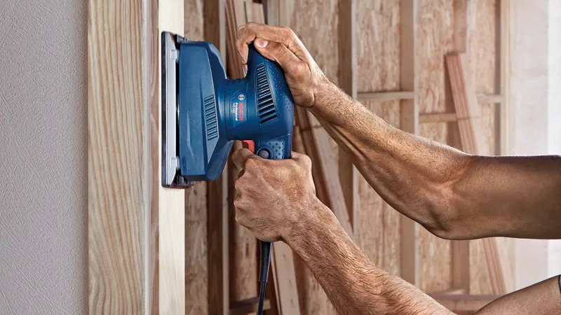 Person sanding a wooden surface with an orbital sander.