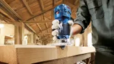 A person wearing safety equipment uses a palm router to shape the edge of a wooden board.