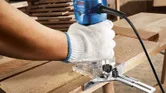 A person wearing safety equipment trims wood with a palm router on a workbench.