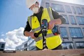 A person wearing safety equipment drills a large hole in wood with a cordless tool.