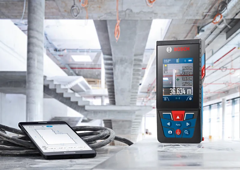 Laser measure and tablet on a construction site floor.