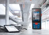 Laser measure and tablet on a construction site floor.