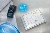 Laser measure and tablet displaying floor plan, next to blue safety helmet.
