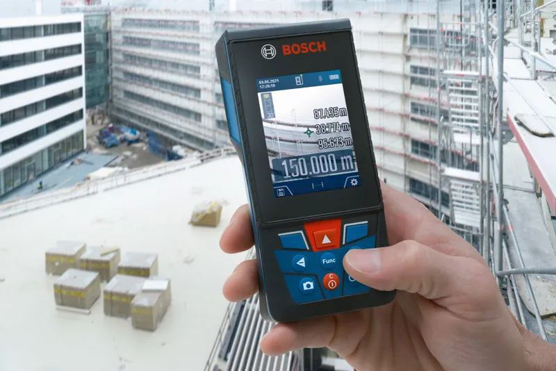 Person holding a laser measure displays building distance measurements at a construction site.