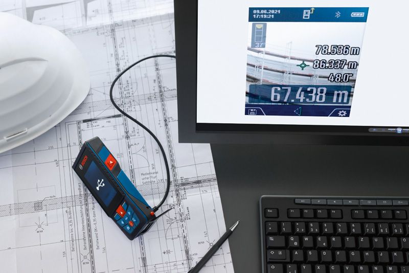 Laser measure connected to a computer on architectural plans beside a hard hat.