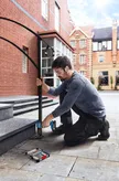 A person wearing safety equipment drills into stone steps, installing a metal handrail.