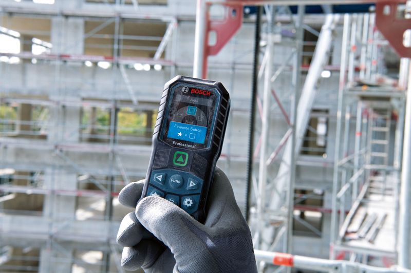 A person wearing safety equipment operates a laser measure at a construction site.
