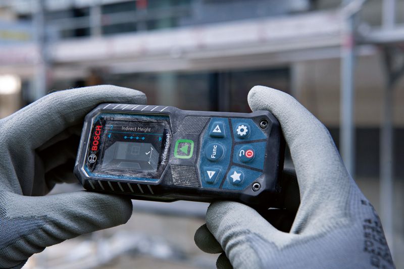 A person wearing safety equipment holds a laser measure on a construction site.