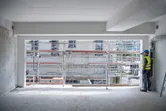 A person wearing safety equipment uses a laser measure to check distance inside a building shell.