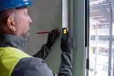 A person wearing safety equipment marks a wall using a laser measure.